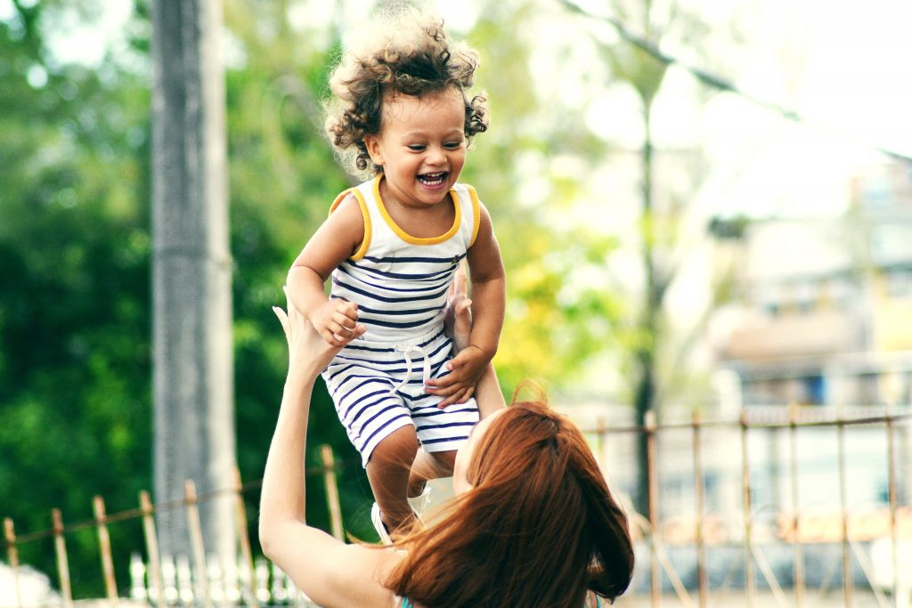Kinder helfen bei Pausen und beim Abschalten von beruflicher Verantwortung.
(Bild zeigt ein lachendes Kind, das gerade von einer erwachsenen Person in die Luft geworfen wird.)